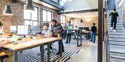 An open-plan workspace with teams working at long shared desks